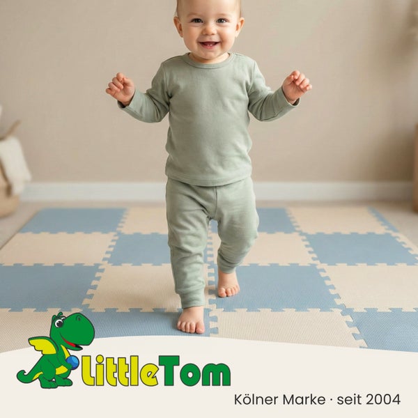 Lächelndes Kleinkind steht auf einer blau-beigen Puzzle-Spielmatte aus Schaumstoff. LittleTom Logo.
