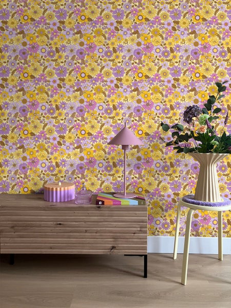 Zimmer mit Holzkommode, Lampe und Stuhl vor einer gelb-lila Blumentapete