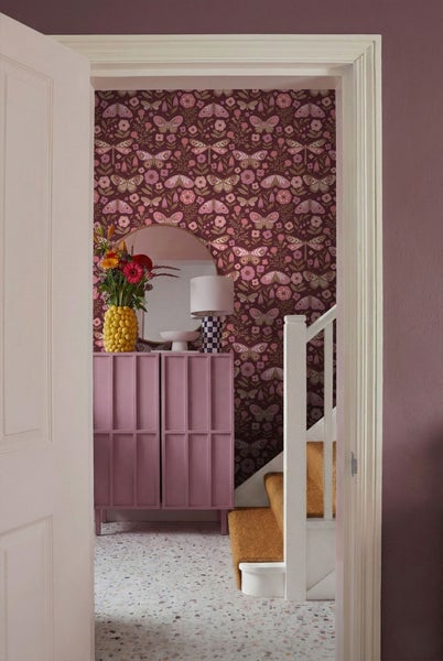 Flur mit Tapete mit Blumen- und Schmetterlingsmuster, Kommode mit Dekoration und Treppe.