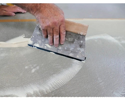 Ein Handwerker verwendet eine Spachtel, um Klebstoff auf einen Untergrund aufzutragen.