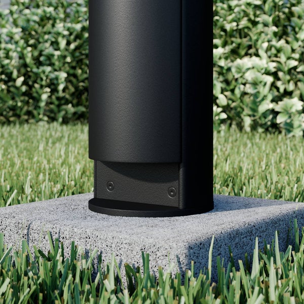 Nahaufnahme des Sockels einer schwarzen Pollerleuchte, montiert auf einem quadratischen Betonfundament im Garten.