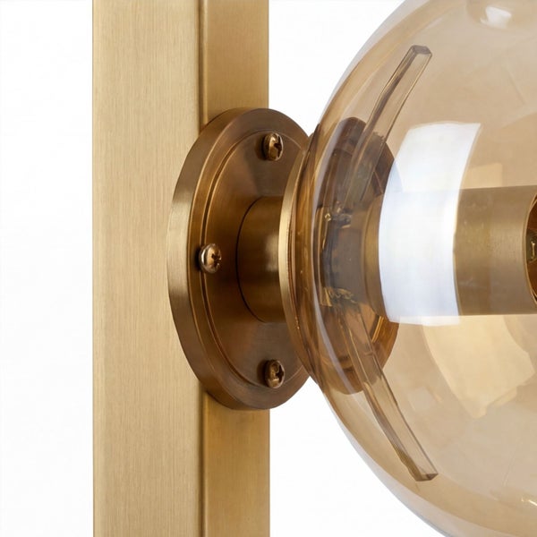 Detailaufnahme einer Wandleuchte mit bernsteinfarbener Glaskugel und Messing-Metallhalterung mit sichtbaren Schrauben.