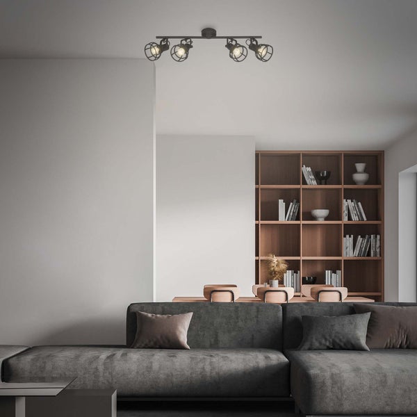 Vierflammige Deckenleuchte im Industrial-Stil mit Drahtkäfigen in einem modern eingerichteten Wohnzimmer mit grauem Sofa und Holzregal.