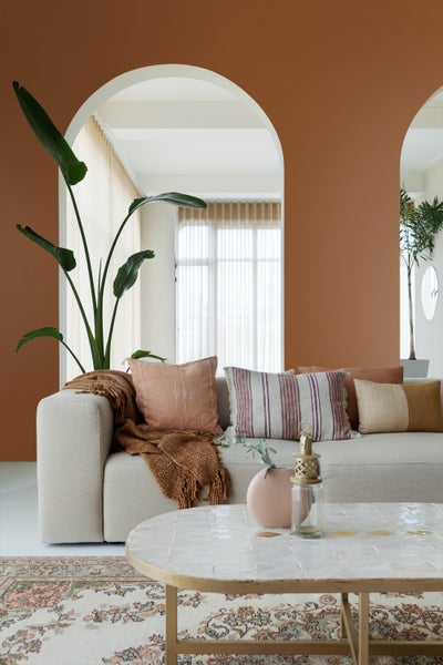 Hell eingerichtetes Wohnzimmer mit modernem Sofa, dekorativen Kissen, großem Rundbogen, einer Zimmerpflanze, Couchtisch und gemustertem Teppich.