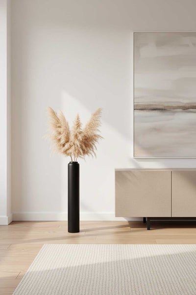 Hohe schwarze Bodenvase mit getrocknetem Pampasgras in einem hellen minimalistischen Wohnzimmer mit beigefarbenem Sideboard und Holzboden.