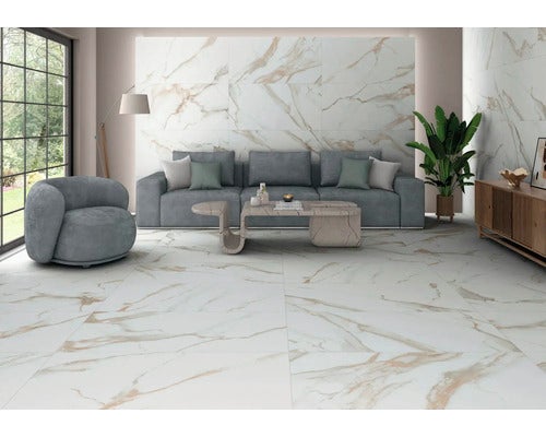 Modernes Wohnzimmer mit großformatigen Fliesen in weißer Marmoroptik an Wand und Boden, grauem Sofa, Sessel und Couchtisch.