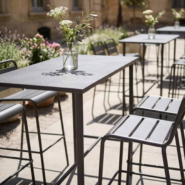 Moderner Stehtisch aus Metall mit passenden Barstühlen auf einer hellen, organisierten Terrasse.