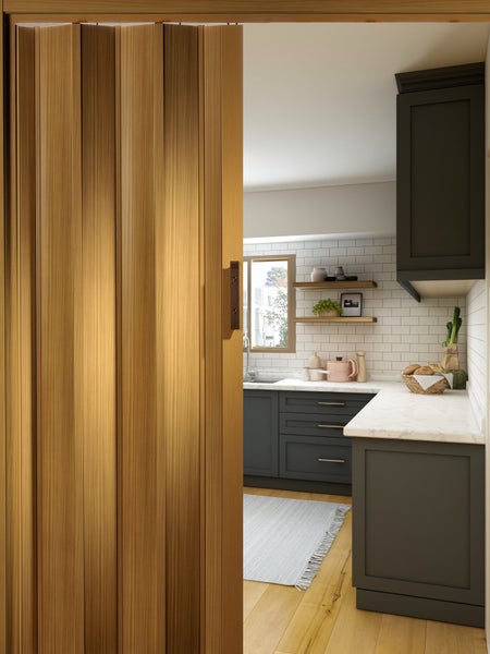 Eine Holztür führt in eine helle Küche mit dunklen Unterschränken und Regalen.