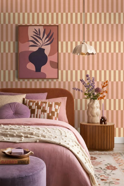 Schlafzimmer mit Vliestapete mit geometrischem Streifenmuster in warmen Tönen, kombiniert mit einem Bett, einem Nachttisch und moderner Dekoration.