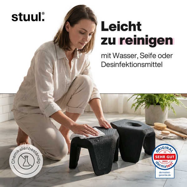 stuul Logo. Eine Frau reinigt den schwarzen Toilettenhocker mit einem Tuch. Er ist leicht zu reinigen, chemikalienbeständig und hautverträglich.