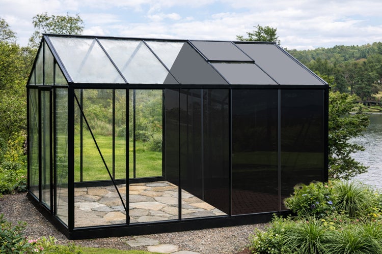 Großes Gewächshaus mit schwarzem Metallrahmen und Steinboden, eine Hälfte mit Klarglas und die andere mit dunklen Paneelen, im Garten.