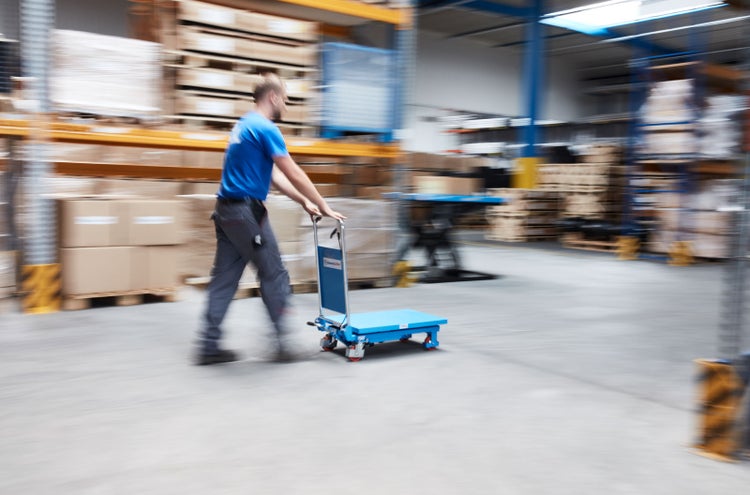 Mann schiebt einen Hubtischwagen in einem Lagerhaus