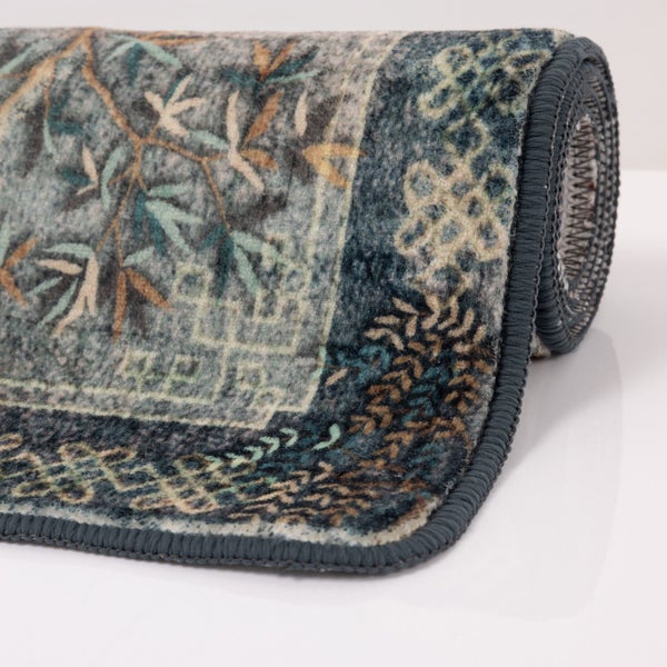 Detailansicht eines aufgerollten Teppichs mit verschlungenem Muster aus Blättern, Ranken und Ornamenten sowie einer gekettelten Kante.