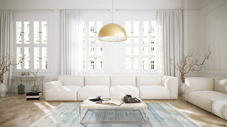 Helles, geräumiges Wohnzimmer mit weißem Sofa, goldenem Pendelleuchten-Design, Holzboden und gemustertem Teppich vor großen Fensterfronten.