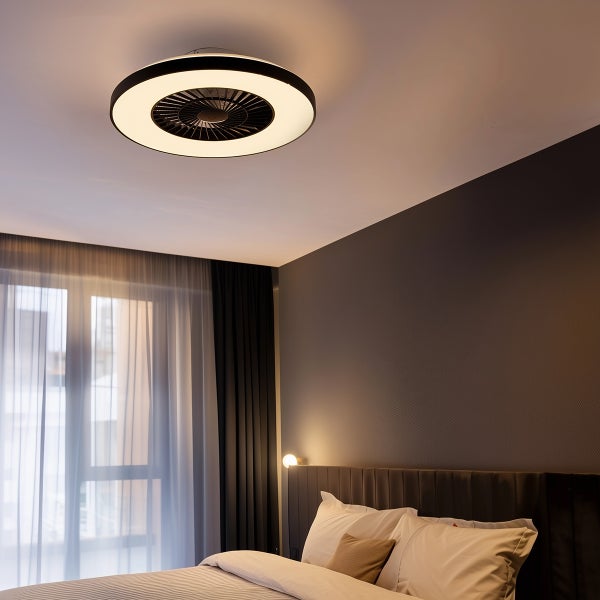Moderner Deckenventilator mit runder LED-Beleuchtung in einem hellen Schlafzimmer über dem Bett.