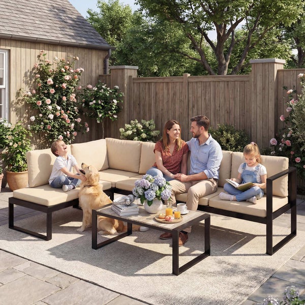 Moderne Garten-Lounge-Ecke aus schwarzem Metall mit beigen Polstern, Couchtisch und Teppich in einem hellen Garten mit Familie und Hund.