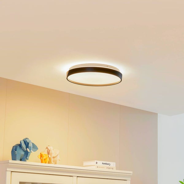 Moderne runde LED-Deckenleuchte in Ringform mit Metallrahmen und Holzoptik, montiert in einem hellen, aufgeräumten Raum über einer Kommode.