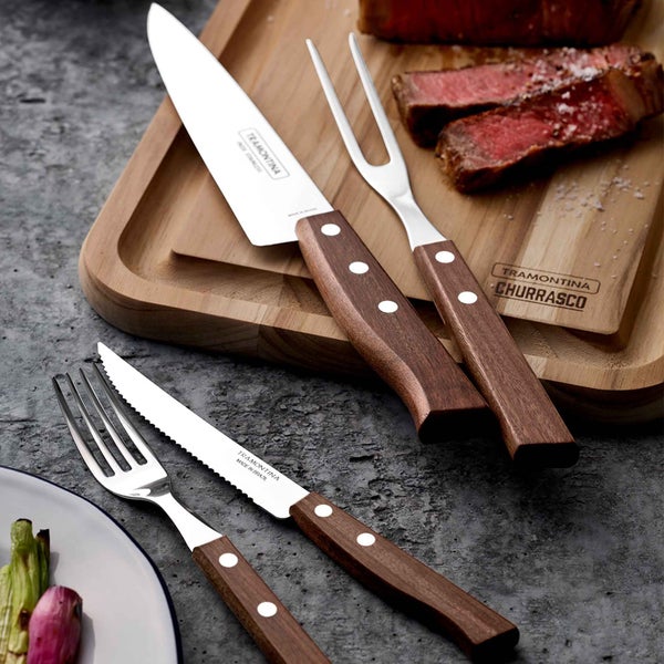 Besteckset mit Steakmessern und Gabeln auf einem Holzbrett mit Fleisch