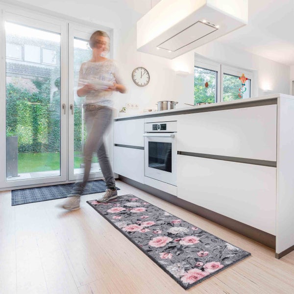 Moderne Küche mit Küchenläufer mit Blumenmuster vor einer weißen Küchenzeile und eine Person in Bewegung.