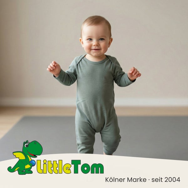 Kleinkind in grünem Strampler stehend auf einer grauen Spielmatte aus Schaumstoff, LittleTom Logo.