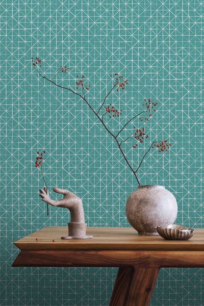 Dekorative Szene mit Vase, Blumenzweig, Handskulptur und geometrischer Tapete auf Holztisch