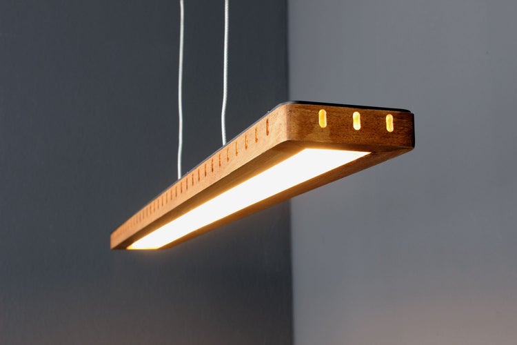 Lineare LED-Pendelleuchte aus Holz mit warmem Lichtpaneel und dekorativen seitlichen Schlitzen.