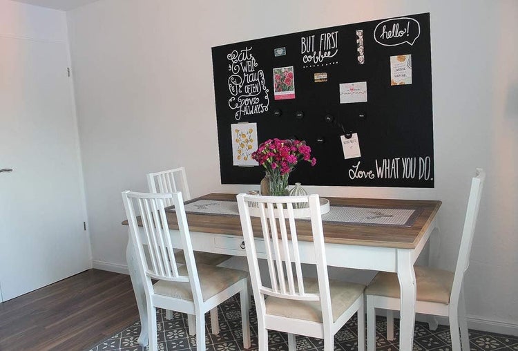 Heller Essbereich mit Esstisch mit Holzplatte, vier weißen Holzstühlen und einer großen schwarzen Magnettafel an der Wand.