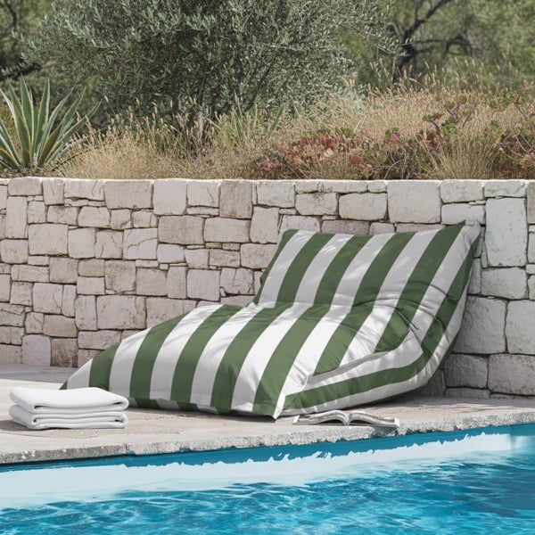 Gestreifter Outdoor-Sitzsack in Grün und Weiß an einem Swimmingpool mit Natursteinmauer, Handtüchern und Gartenpflanzen.