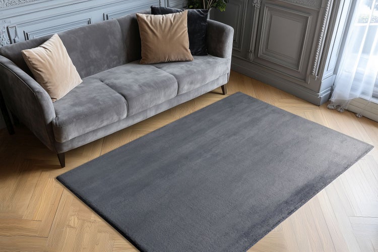 Rechteckiger Teppich vor einem Sofa auf Parkettboden in einem elegant eingerichteten Wohnzimmer mit Wandvertäfelung.
