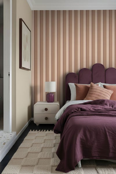 Schlafzimmer mit lila Bett, Nachttisch und gestreifter Tapete
