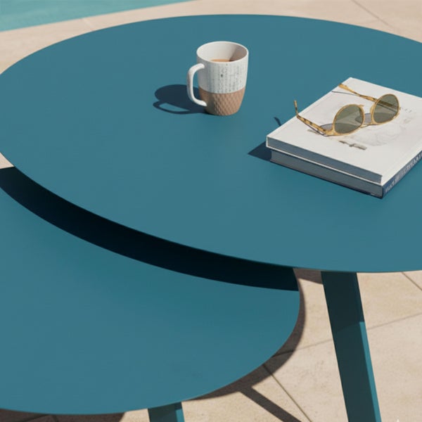 Zwei runde Satztische für den Garten aus Metall in Blaugrün mit einer Tasse, einem Buch und einer Sonnenbrille auf der Tischplatte.