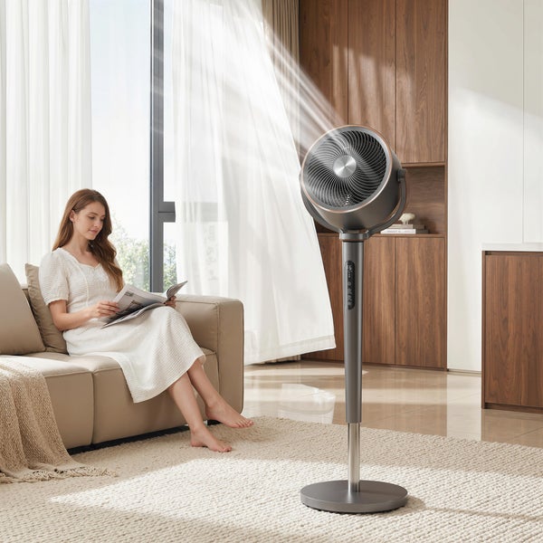 Moderner Standventilator in einem hellen Wohnzimmer mit einer Frau auf dem Sofa, Holzmöbeln und großem Fenster, organisierte Atmosphäre.