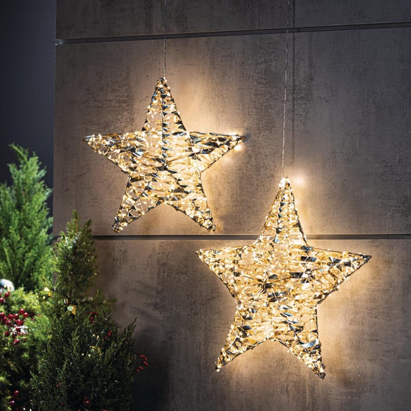 Zwei leuchtende Weihnachtssterne als Hängedekoration mit integrierter LED Beleuchtung vor einer strukturierten Wand mit Tannenbaum.
