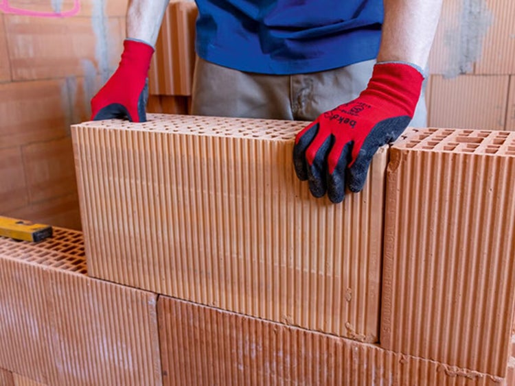 Handwerker beim Mauern mit Ziegelsteinen und Schutzhandschuhen auf einer Baustelle