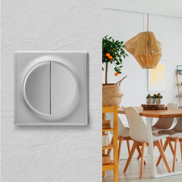 Doppelwippschalter an einer Wand neben einem hellen Wohnzimmer mit Esstisch und Holzmoebeln.