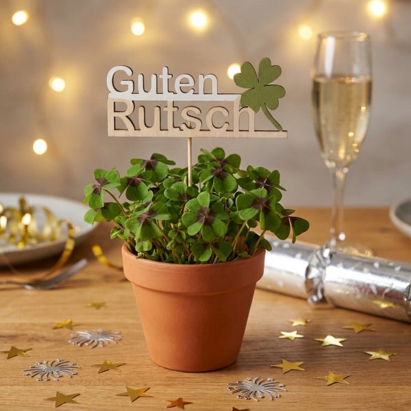 Glücksklee in einem Tontopf mit einem Holzstecker Guten Rutsch und einem Kleeblatt, dekoriert für Silvester auf einem Tisch.