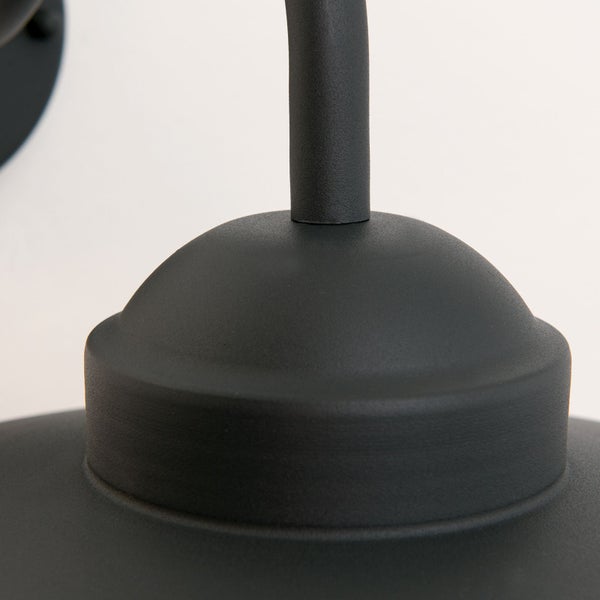 Detailansicht einer matten Metall-Wandleuchte mit gebogenem Arm und kuppelförmiger Abdeckung.