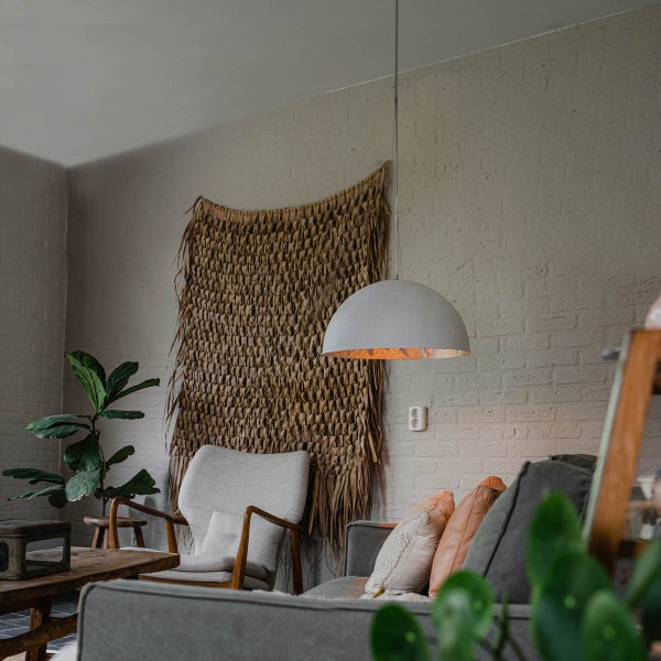 Wohnzimmer mit Sofa, Sessel, Zimmerpflanze, Wandteppich und halbrunder Hängelampe