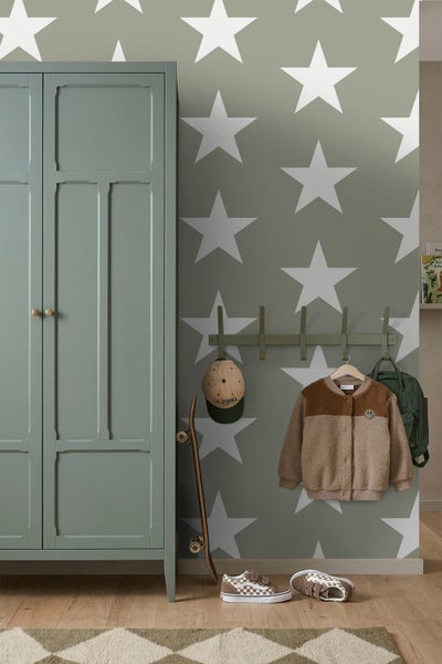 Vliestapete mit großen weißen Sternen auf grünem Hintergrund in einem Kinderzimmer mit Kleiderschrank und Garderobe.