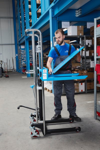 Mann in Arbeitskleidung bedient einen manuellen Hochhubwagen aus Metall in einem hellen, organisierten Lager mit Regalsystemen.