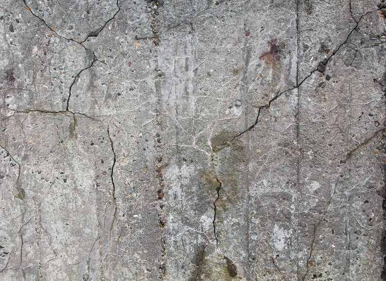 Nahaufnahme einer verwitterten Betonwand mit sichtbaren Rissen und grober Steinstruktur.