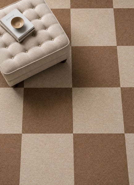 Teppichfliesen im Schachbrettmuster in Beige und Braun mit einem gepolsterten Hocker in einem hellen, organisierten Wohnraum.