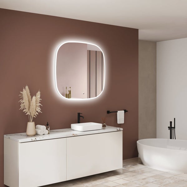 Modernes Badezimmer mit beleuchtetem, abgerundetem Wandspiegel, Waschbecken auf Unterschriftelement mit Marmorplatte und freistehender Badewanne.