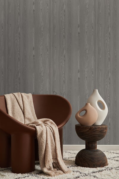 Raumszene mit grauer Holzoptik-Tapete, Sessel mit Decke und zwei Vasen auf einem Hocker