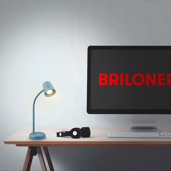 Moderne blaue Schreibtischlampe auf einem Holzschreibtisch neben einem Computermonitor mit Briloner Logo Tastatur und Kopfhörern