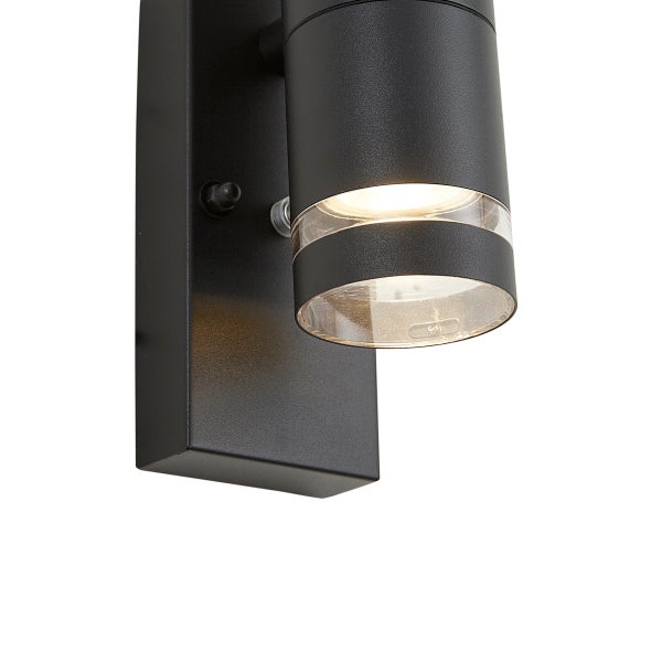 Schwarze Außenwandleuchte mit zylindrischem Kopf und Bewegungsmelder, Licht strahlt durch einen transparenten Ring nach unten.