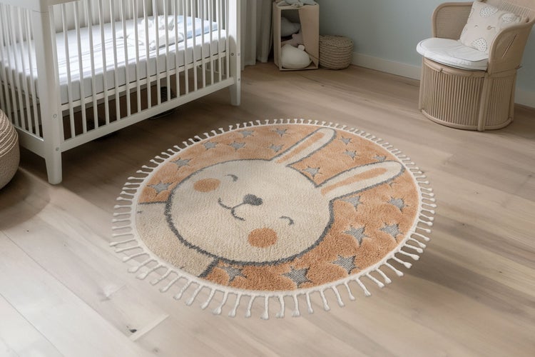 Runder Kinderteppich mit Hasenmotiv und Sternenmuster sowie Fransenrand in einem gemütlich eingerichteten Kinderzimmer.