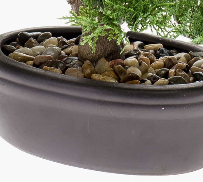 Detailansicht einer künstlichen Pflanze in einer grauen Keramikschale mit Dekosteinen und grünem Nadelwerk.