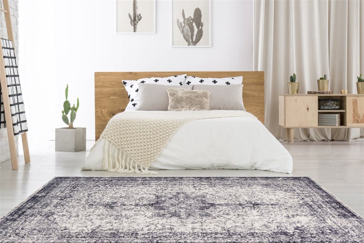 Ein moderner Teppich mit Vintage Muster liegt in einem hellen Schlafzimmer mit Holzbett und Sideboard im Hintergrund.