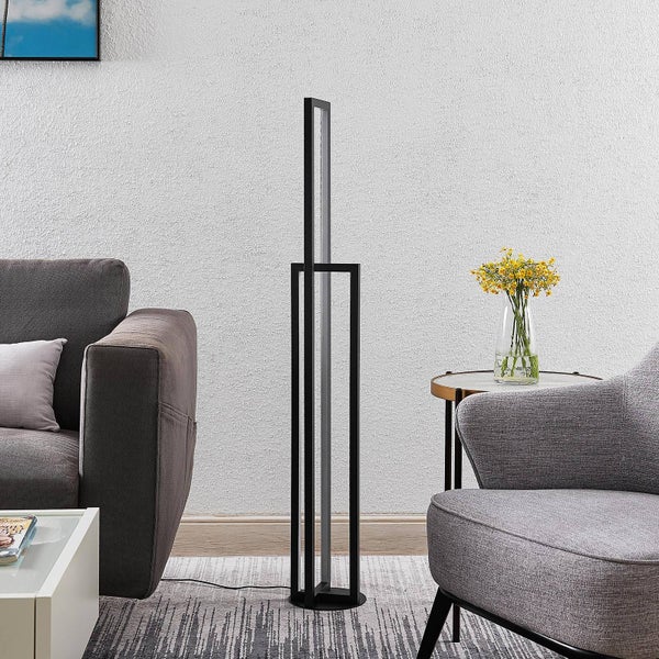 Moderne schwarze LED-Stehleuchte in minimalistischem Rahmendesign in einem hellen Wohnzimmer zwischen einem grauen Sofa und einem Sessel.